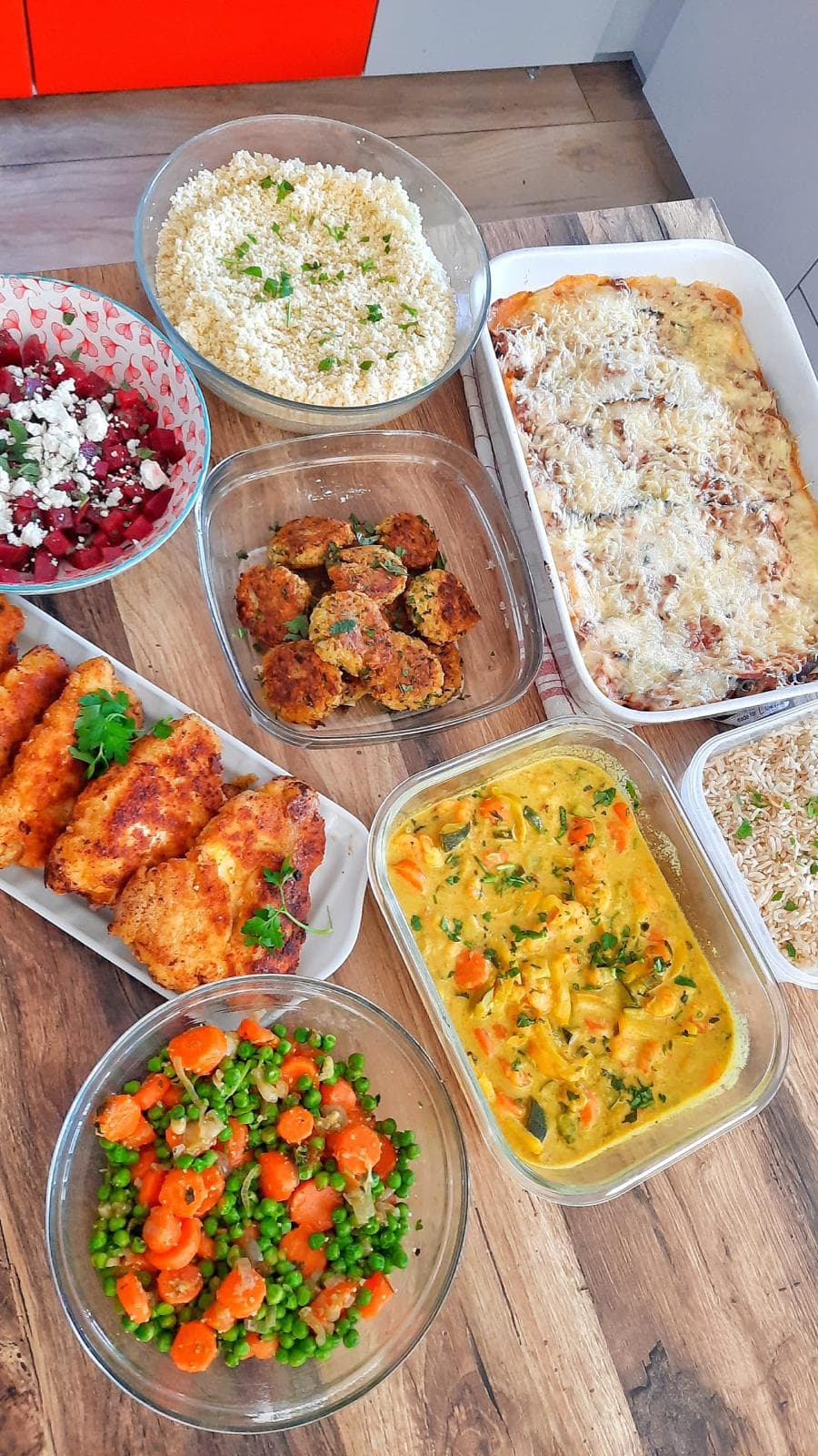 Une semaine de dîners en barquettes : boulettes, curry de légumes, gratin, riz, houmous et poêlée, sur une table en bois